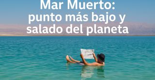 Persona flotando en el Mar Muerto leyendo un periódico, con agua turquesa y formaciones salinas al fondo